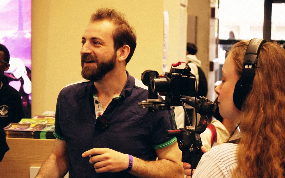 Interview filmée en convention, cadreuse casquée au premier plan.